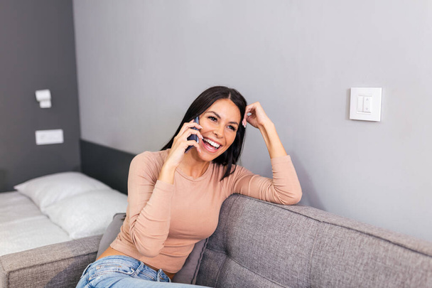 Smiling beautiful woman talking on the phone at home, happy young girl holds cellphone making answering call, attractive girl having pleasant conversation chatting by mobile with friend - Foto, immagini