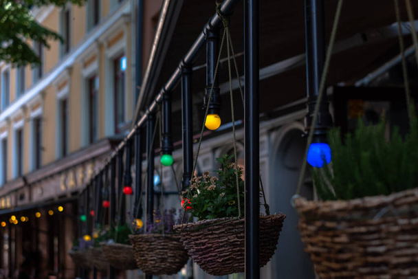 Close-up of row of wicker flower pots at the cafeteria facade. Blurred colorful decorative lamps. Blurred background. Selective focus - Φωτογραφία, εικόνα
