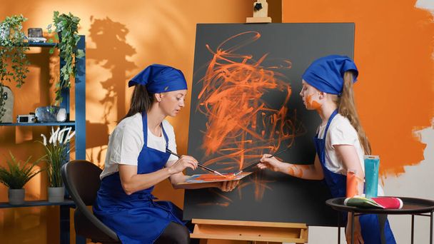 Woman and girl using aquarelle palette to paint on canvas, learning to create artwork design with artistic tools and equipment. Painting masterpiece with watercolor dye and paintbrush. Tripod shot. - Foto, afbeelding