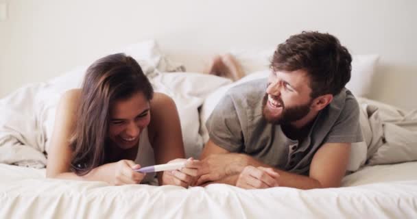 Happy, wow and surprised couple with pregnancy test at in bed at home. Man and woman excited for good news and excited for child and to be parents while relax, hug and laugh in bedroom together. - Filmati, video