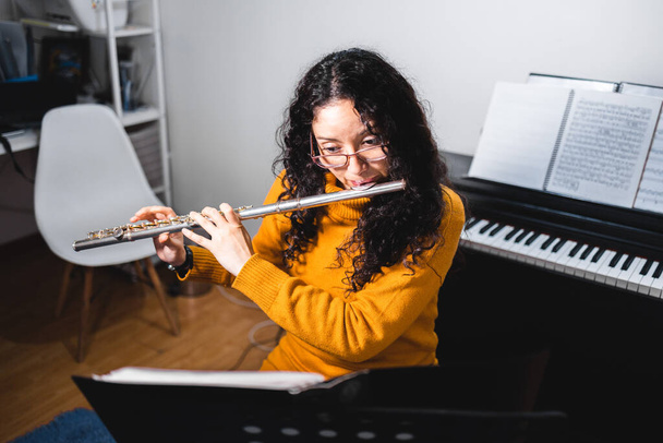 Brunette woman wearing a yellow sweater, and playing a transverse flute. High quality photo - Foto, imagen