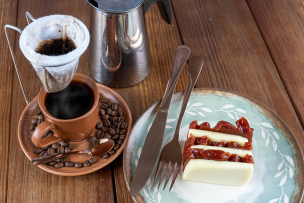 Guava sweet and curd cheese slices next to cutlery, cup, beans and cloth coffee filter. - Φωτογραφία, εικόνα