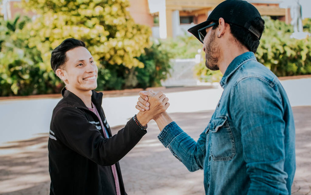 Two people shaking hands on the street. Two teenage friends shaking hands at each other outdoors. Concept of two friends greeting each other with handshake on the street. - Photo, image