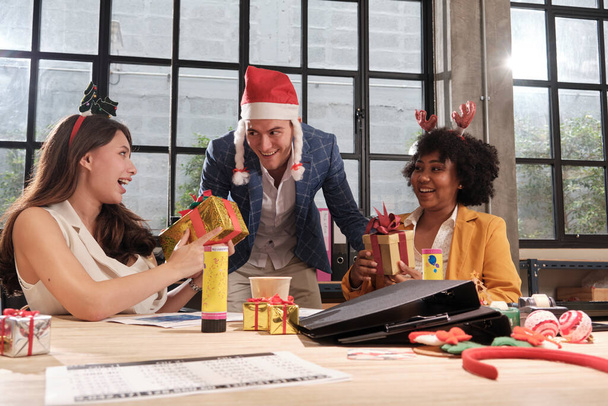 Male Caucasian boss in Santa hat surprise female coworkers team by giving gifts at business office in Christmas festival party and new year celebrate before company holiday, enjoyment and happiness. - Foto, immagini