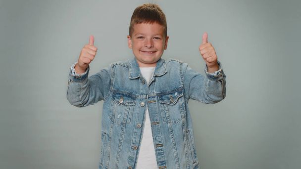 Like, yes. Toddler young teen boy raises thumbs up agrees with something or gives positive reply recommends advertisement likes good. Children teenager child kid isolated on gray studio background - Foto, Bild