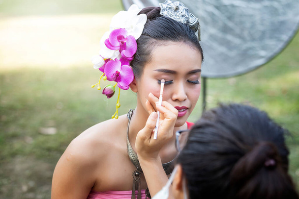 Maquillaje artista que hace hasta delineador de ojos a la mujer tailandesa con ropa tradicional tailandesa - Foto, Imagen