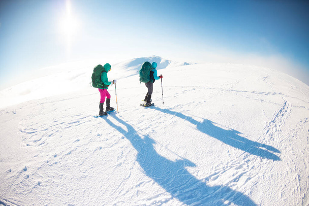 Két nő hótalpban sétál a hóban, télen túráznak, télen két ember a hegyekben, túrázó felszerelésben. - Fotó, kép