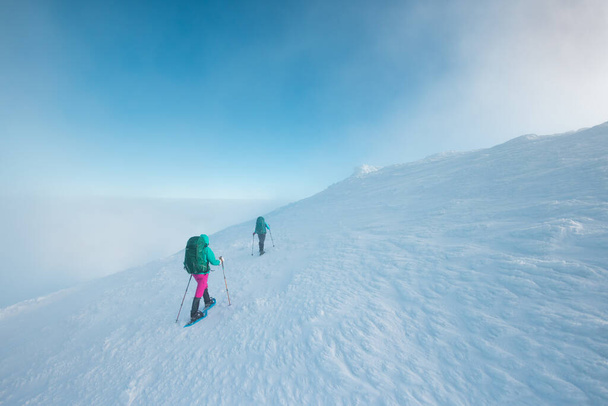 climbers climb the mountain. two girls in snowshoes walk in the snow. hiking in the mountains in winter. - 写真・画像