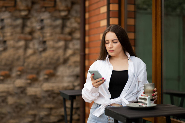Привлекательная брюнетка в уличном кафе, читающая смс с телефона. Копирование пространства - Фото, изображение