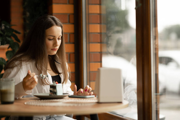 Charmante ernsthafte Frau liest gute Nachrichten auf dem Handy, während sie es sich im Café gemütlich macht, kaukasische Frau betrachtet ihre Fotos auf dem Handy, während sie sich in der Freizeit im Café entspannt. Kopierraum - Foto, Bild