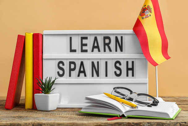 Board with text LEARN SPANISH, flag, eyeglasses and books on table against beige background - Fotoğraf, Görsel