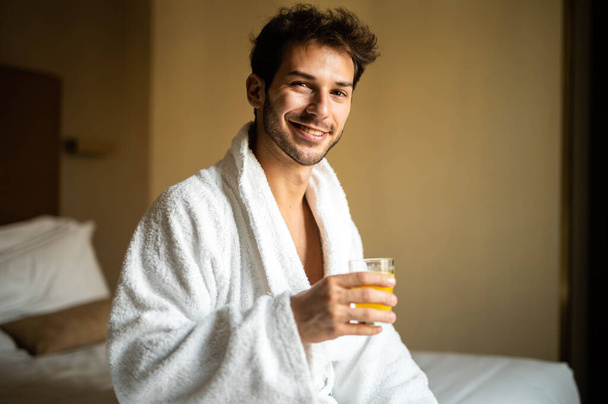 Portré h fiatal férfi fehér fürdőköpenyben ivás narancslé - Fotó, kép