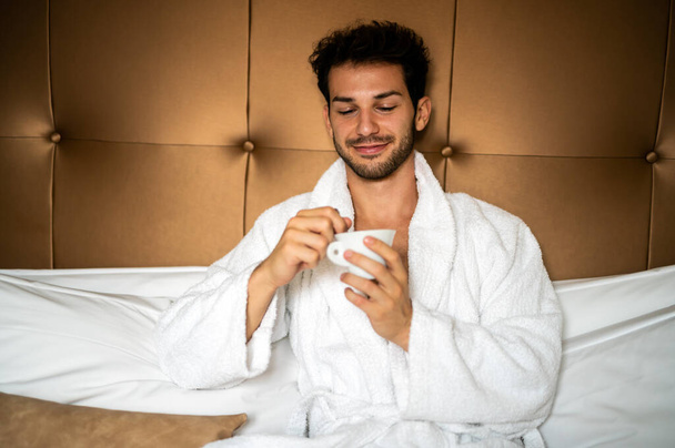 Young handsome man drinking morning coffee in bathrobe - Fotoğraf, Görsel