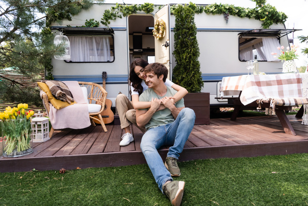 Smiling woman embracing boyfriend on terrace near camper outdoors  - Foto, imagen