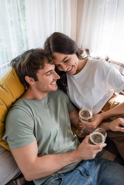 High angle view of cheerful young couple holding glasses of wine on bed in camper van  - Foto, imagen