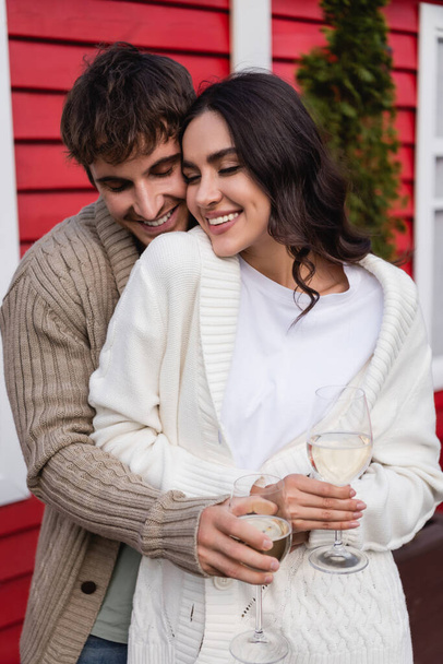 Smiling couple in cardigans holding glasses of wine outdoors  - Φωτογραφία, εικόνα
