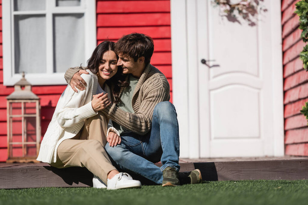 Cheerful young couple in cardigans hugging on terrace of house  - Foto, afbeelding