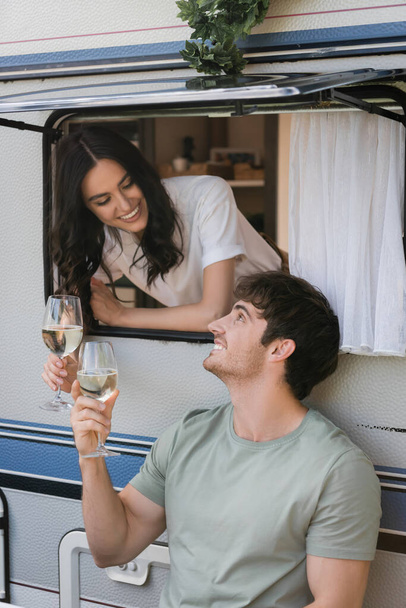 Smiling man holding glass of wine near girlfriend in camper van  - Valokuva, kuva