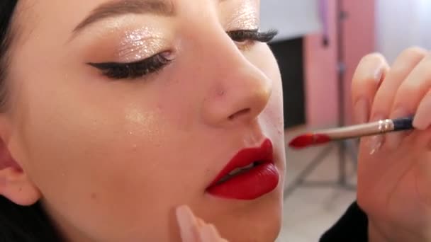 Bright lip makeup, big beautiful lips are painted with red lipstick with a special brush in a beauty salon. Professional make-up. Makeup with black arrow. - Footage, Video