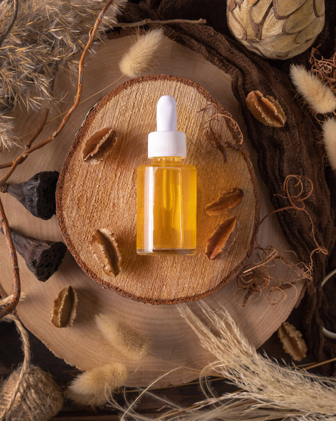 Dropper bottle with yellow liquid on wood near natural boho decorations top view, cosmetic packaging mockup. Skincare beauty product, serum or essence. Bohemian eco friendly flat lay with dried leave - Fotografie, Obrázek