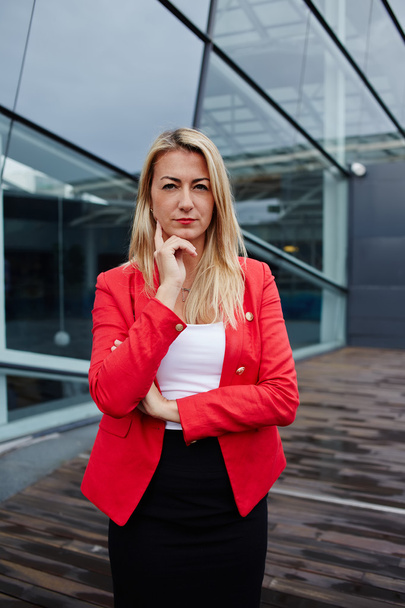 Portrait of confident young businesswoman in suit reflectively looking to the camera, executive woman carefully listen to the employee, confident business woman in red jacket standing near office - Zdjęcie, obraz