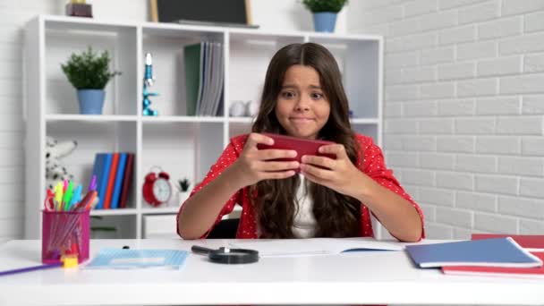 School child play smartphone games making winning gesture pretending doing homework at desk, mobile gaming. - Filmagem, Vídeo