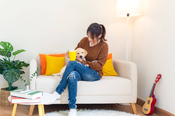 Young asian woman cheerful and relax time with sweet puppy dog pet and owner having good time together at living room at home. Female drinking coffee with pet friendship.  Lifestyle concept - Foto, immagini
