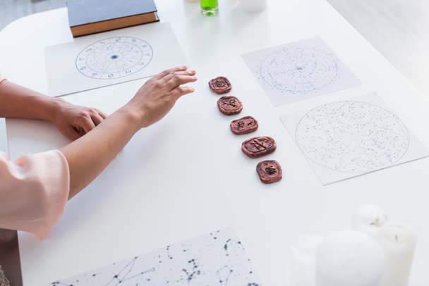 high angle view of cropped astrologist near star charts and clay runes on table - Foto, imagen