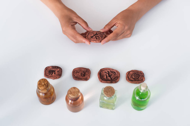 top view of partial fortune teller holding clay rune near jars with essential oils - Foto, Imagem