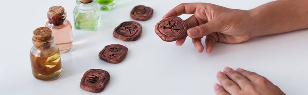 cropped view of predictor holding clay rune near bottles with essential oils, banner - Zdjęcie, obraz
