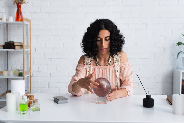 brunette astrologist touching magic sphere near tarot cards and diffuser with aroma stick - Fotó, kép