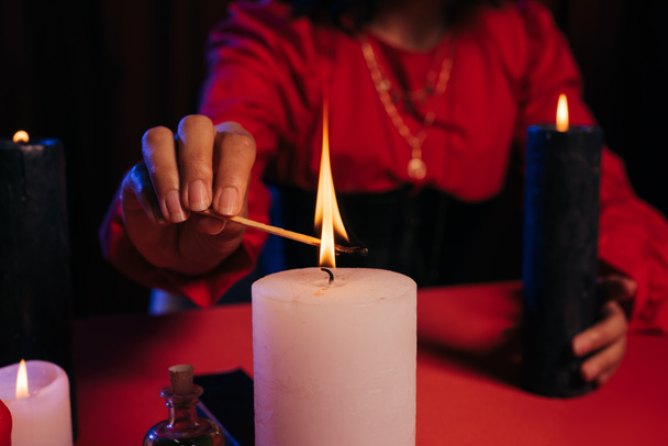 cropped view of blurred fortune teller lighting palo santo stick near burning candle isolated on black - Fotografie, Obrázek