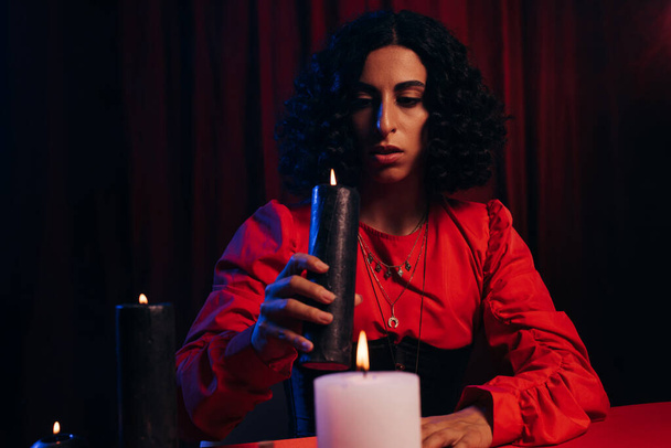 young brunette oracle holding burning candle on dark background - Photo, Image