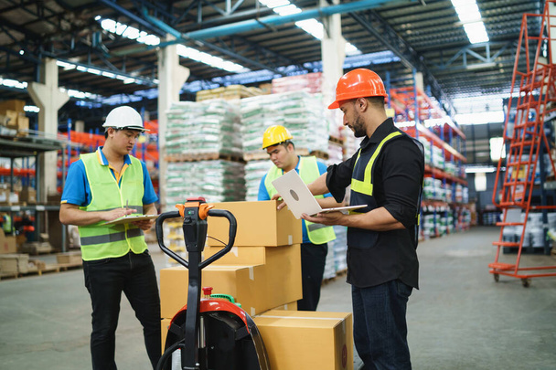 Manager man using laptop check stock cardboard on forklift and co-worker at warehouse. Worker wearing high visibility clothing and hard hat, helmet to checking count up goods or boxes for delivery. - Zdjęcie, obraz