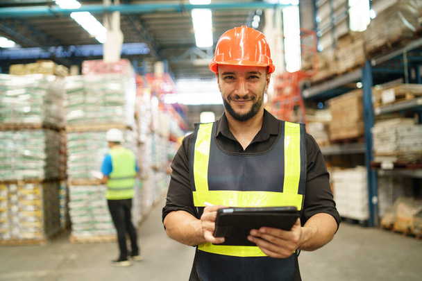 Professional manager man employee using tablet check stock working at warehouse. Worker wearing high visibility clothing and a hard hat, helmet and checking and count up goods or boxes for delivery. - Foto, afbeelding