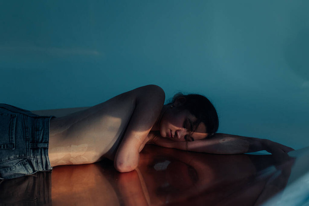 Beautiful young woman with amputee arm and scars from burn on her body poses lying topless. There is visible her reflection on surface. The concept of a fulfilling life of persons with disabilities. - Zdjęcie, obraz
