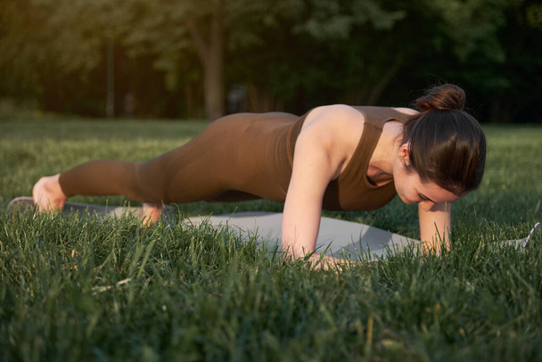 Athletic woman doing yoga in the park while standing in a plank position. The concept of a healthy lifestyle and life extension - Φωτογραφία, εικόνα