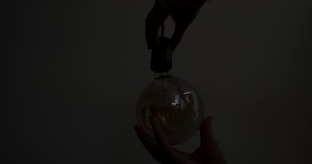 Male hands screw a light bulb into a socket in a dark room. Close-up. Yellow bright light, the light bulb on the wire lights up. High quality 4k footage - Video, Çekim