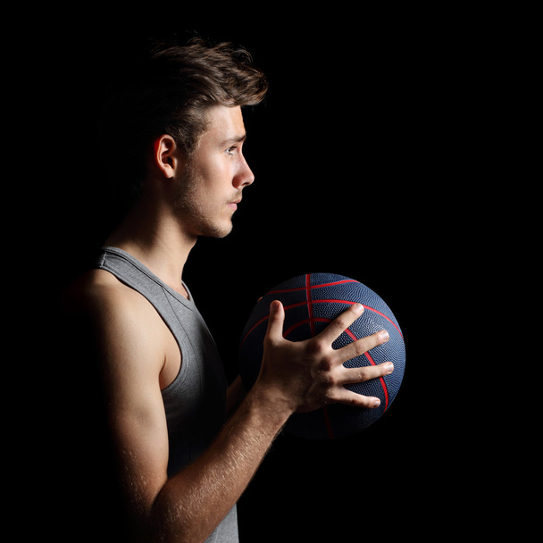 Basketball player holding ball on black - Foto, afbeelding