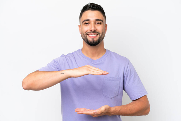 Junger arabischer gutaussehender Mann isoliert auf weißem Hintergrund mit einem imaginären Kopierraum auf der Handfläche, um eine Anzeige einzufügen - Foto, Bild