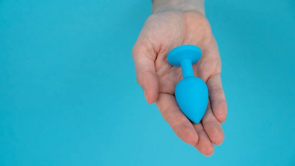 Woman holding a blue anal plug on a blue background - Foto, Imagen
