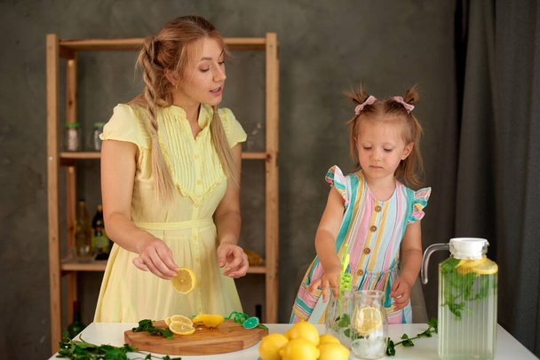 little girl helps mom in kitchen to prepare summer cold drink lemonade - Foto, immagini