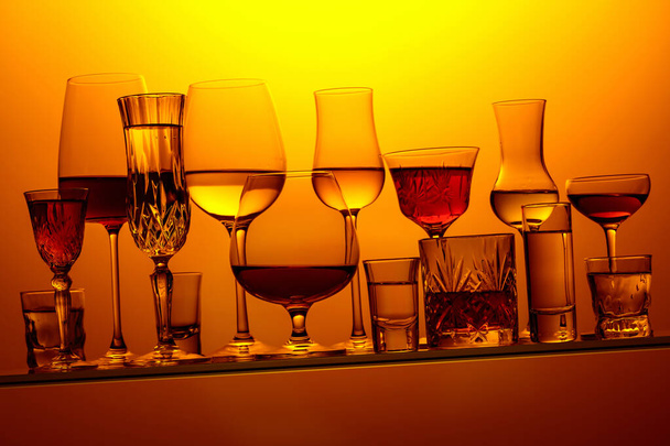 Various alcoholic drinks in a bar on a tilted glass shelf. Yellow background. - Foto, afbeelding