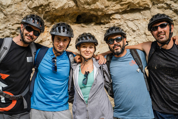 group of people portrait of caucasian friends men and woman standing in front of electric bikes e-bike while taking a brake during off-road outdoor ride in sunny summer day wear protective helmet - Foto, Bild