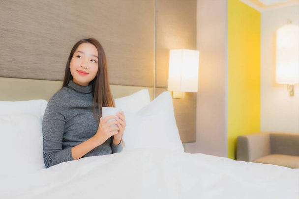 Portret piękna młoda azjatycka kobieta z filiżanką kawy na łóżku we wnętrzu sypialni - Zdjęcie, obraz