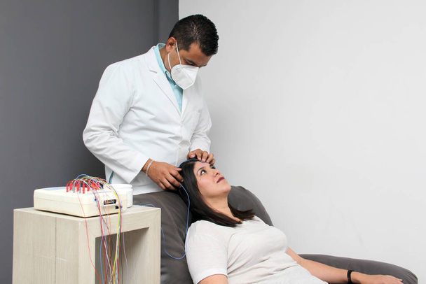 Latin neurologist medical specialist doctor measures the head of his Latin woman patient to stick the electrodes and check the brain activity with an electroencephalogram EEG - Foto, imagen