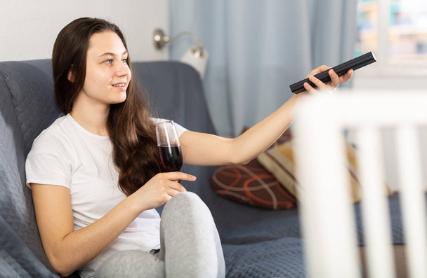 Young woman relaxing on sofa at home, drinking wine and watching tv - Фото, изображение