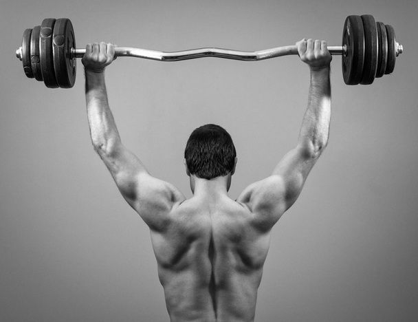 Muscular man doing exercises with barbell. Back view. Black and white. - Photo, Image