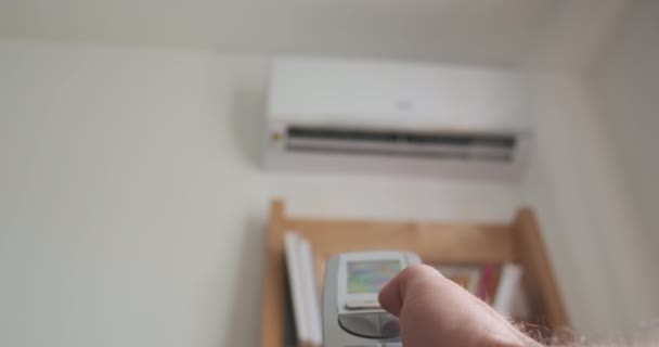 Mans hand turns off the air conditioner using a remote control. Close-up, blurred air conditioner hanging on the wall. High quality 4k footage - Кадры, видео