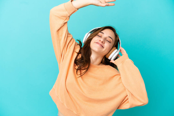 Giovane donna caucasica isolata su sfondo blu ascoltare musica e ballare - Foto, immagini